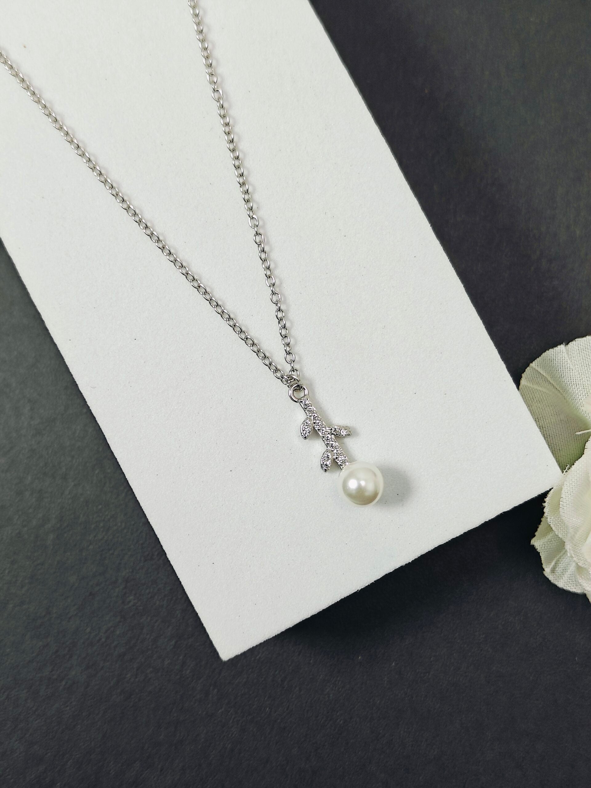 Silver necklace with a pearl pendant on a white card, with a white rose in the corner.